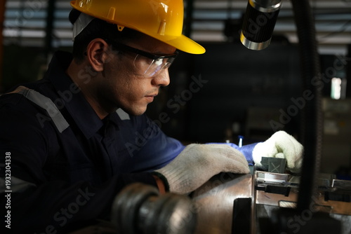 Asian male engineer foreman, in charge of operating automatic machinery, is currently watching and using tools to inspect the quality of metal cutting machines and automotive parts in a car parts manu