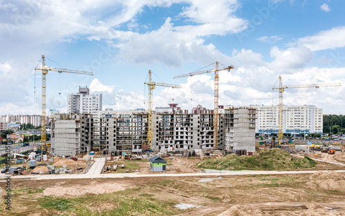 city residential area under construction. building site with cranes on blue cloudy sky background. aerial drone photo.