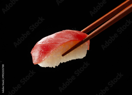 Close up of chopsticks holding maguro tuna nigiri sushi on black background