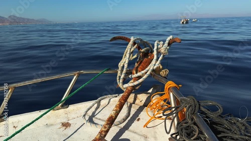 Rusty anchor on bow of authentic fishing boat in deep blue sea