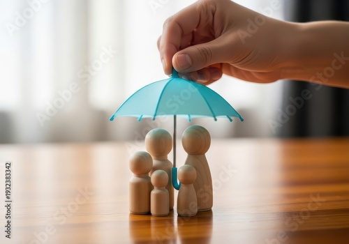 A hand holding an umbrella over a wooden family figurine set on a wooden table.