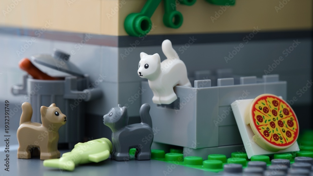 Naklejka premium Tambov, Russian Federation - July 02, 2025 Lego cats standing behind a building near a crate and trash can with a pizza and fish