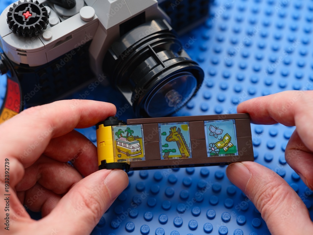 Fototapeta premium Tambov, Russian Federation - February 20, 2026 Person hands holding a toy film strip from the LEGO Creator 3in1 Retro Camera building set with a vintage-style brick-built camera in the background.