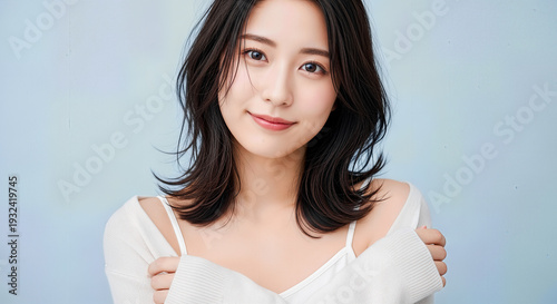 Happy young Asian woman with short hair wearing white sweater smiling and looking at camera isolated on clean light blue background