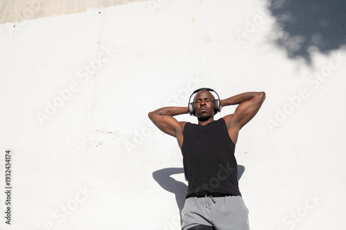 Φωτογραφία Man enjoying music and resting against a white wall after exercising