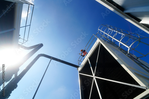 Foto Worker inspecting industrial cooling tower structure against a clear blue sky