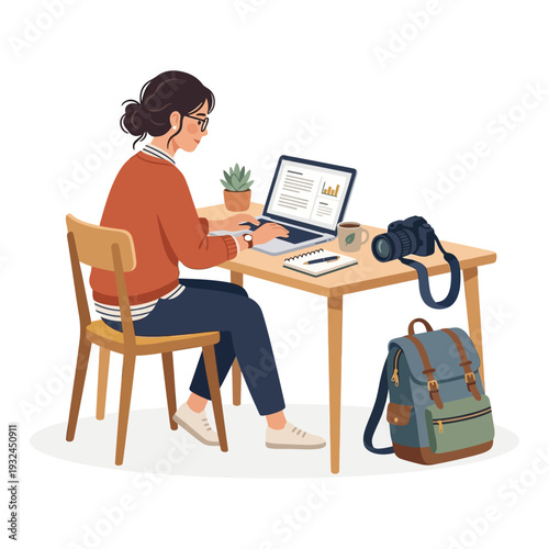 Woman sitting at desk working on laptop surrounded by photography equipment and personal items in a relaxed office setting