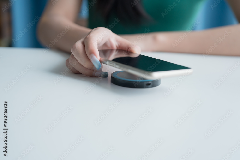Fototapeta premium Charging mobile phone battery with wireless charging device in the table. Smartphone charging on a charging pad. Mobile phone near wireless charger Modern lifestyle technology.