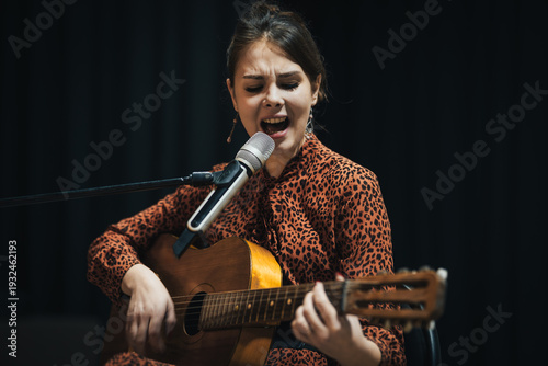 Foto Young beautiful woman on stage in spotlight lights playing guitar and singing fo