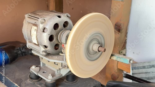 Bench grinder sharpening wheel spinning at high speed, close-up of abrasive sharpening tool in a workshop.
