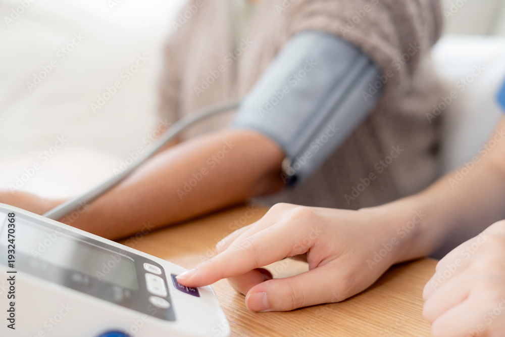 Fototapeta premium Asian woman nurse measuring blood pressure senior patient, medical checking for hypertension monitoring, caregiver support elderly woman with arterial blood pressure device, routine health checkup.