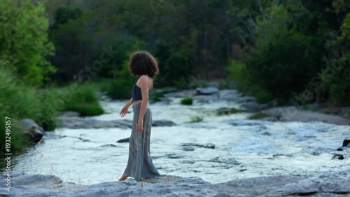 A Woman Gracefully Dancing by the Riverbank, Embracing Nature's Serenity and Motion in a Beautiful Outdoor Setting Surrounded by Lush Greenery and Gentle Waters