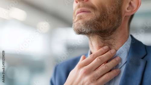 Businessman suffering from sore throat and touching neck in office.
