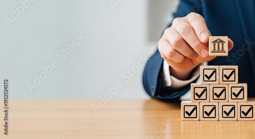 Business hand placing bank icon wooden block, checkmark pyramid on wooden desk, financial compliance approval Concept