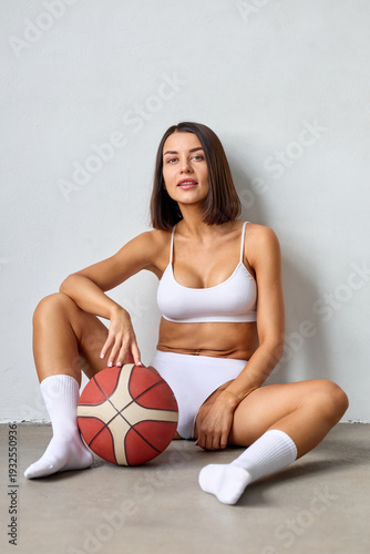 A tasteful fusion of athleticism and fashion is on display as a woman dons white lingerie and holds a basketball in a studio shot.