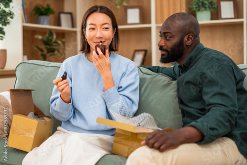 A multiracial couple relaxes on the couch, reviewing an online order as they unpack a freshly delivered perfume.