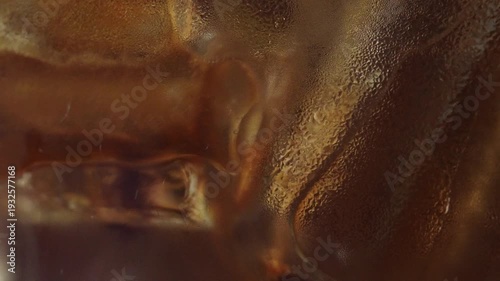 4K Macro close-up of black coffee being poured over ice cubes in a glass, Rich brown liquid flows through clear ice with dynamic splash and texture ideal for refreshing beverage and cafe concepts.