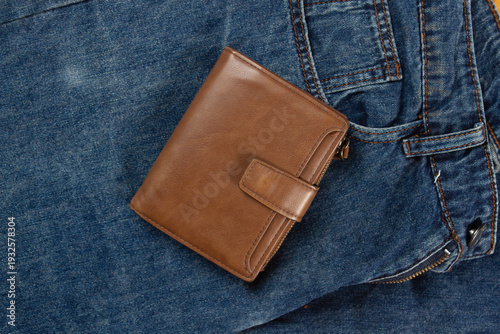 A brown men's wallet lies on a pair of blue jeans.