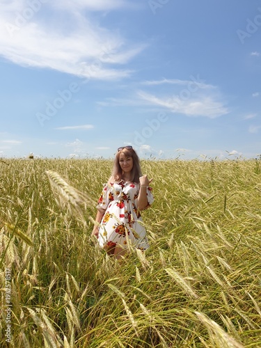 Young woman standing in a golden wheat field under blue sky in summer countryside