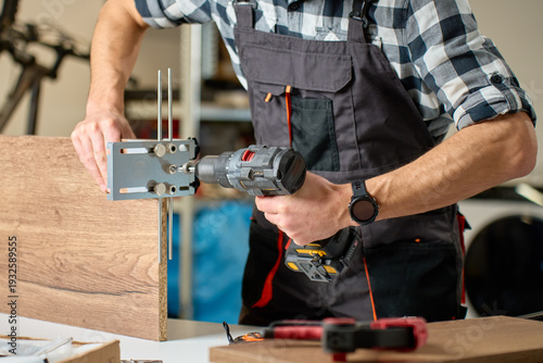 Fotografie Close-up of carpenter drilling hole in wooden board using drill and metal jig tool