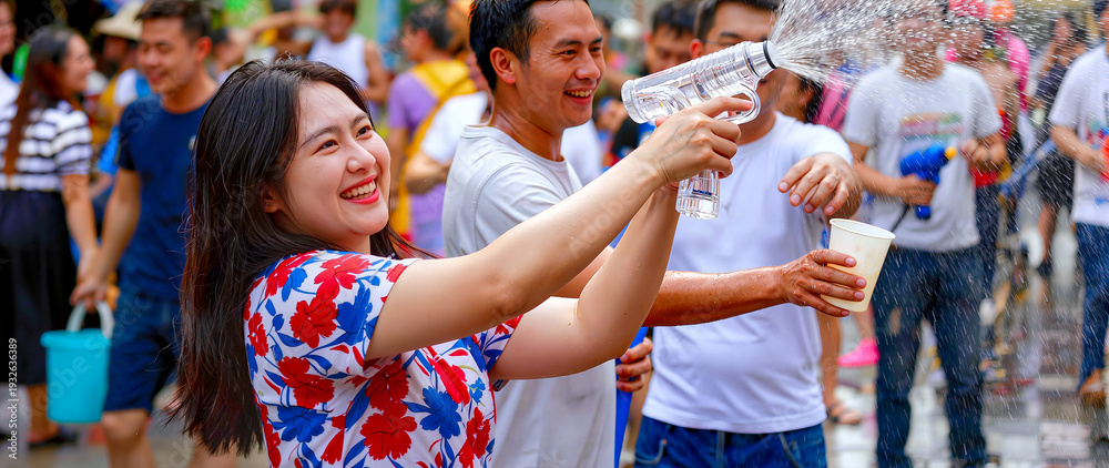 Obraz premium Cheerful young Asian woman enjoying Songkran water festival in Thailand, playing with water gun among crowd, traditional Thai New Year celebration, , panoramic banner with copy space.