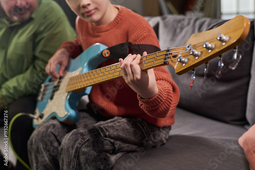 Billede på lærred Caucasian child playing electric bass guitar on sofa, focusing on hand positioni