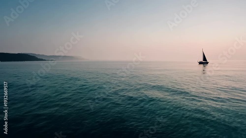 Sailboat gliding across calm waters at dusk, with gentle waves reflecting the soft colors of the sky and distant shoreline visible in the background