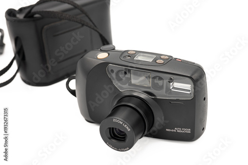 Front view of a vintage black 35mm compact film camera with its zoom lens fully extended, featuring a built-in flash and original case, isolated on a white background.