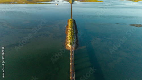 Aerial view of a narrow strip of land bisecting the tranquil lagoon, connected by a weathered bridge under a serene sky, Knysna, Western Cape, South Africa.