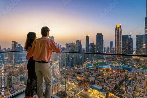 A elegant couple looks from their balcony at the illuminated skyline of downtown Dubai, UAE, during dusk