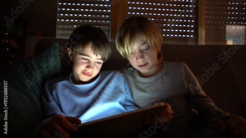 Two boys playing videogames on a tablet at night