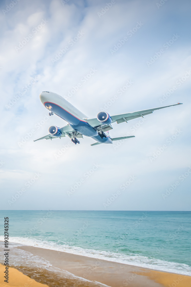 Fototapeta premium Skyline view of an airplane flying over a beach with ocean waves and distant clouds during day light hours