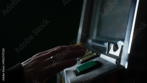 A gambler plays a retro slot machine, inserting a coin and pressing the Start button. The man hand presses the button and celebrates his victory. Slow motion.