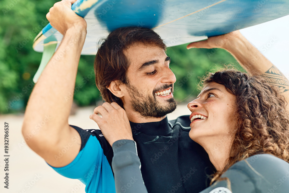 Fototapeta premium Portrait of a young couple surfing at the beach, holding surfboards, having fun together ocean waves, healthy life holidays adventure concept