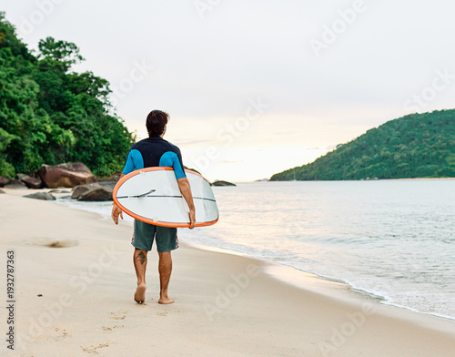 Photography Portrait of a young man surfing at the beach, holding surfboard, ocean waves, he