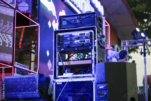 Blue stage lighting illuminates professional sound system with speaker, amplifier, and equipment rack for an energetic outdoor music festival or night concert celebration