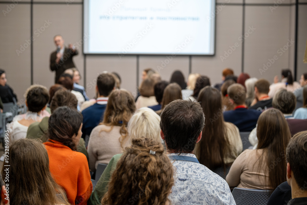 Obraz premium Business conference presentation with audience focused on speaker and projected slides, collaborative learning atmosphere, professional networking and knowledge sharing.
