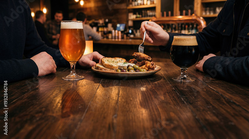 Two glasses of craft beer with appetizers on wooden table in cozy pub, warm light and casual dining atmosphere with friends.