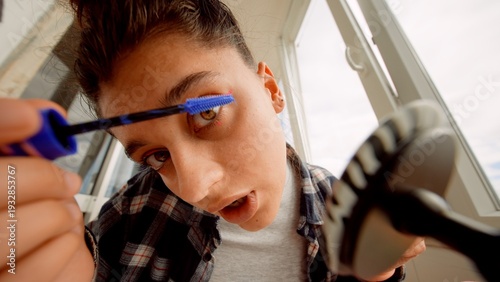 Woman expertly applying vibrant blue mascara to her lashes