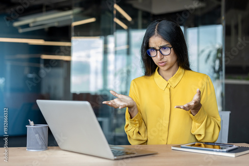 A young Indian businesswoman is sitting at her office desk and enjoying a video call on her laptop
