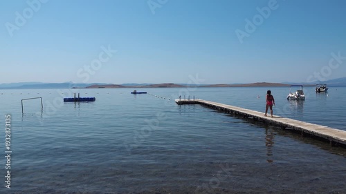 The little girl is walking towards the sea. A child entering the calmly rippling water on a bright summer day. A peaceful holiday scene.