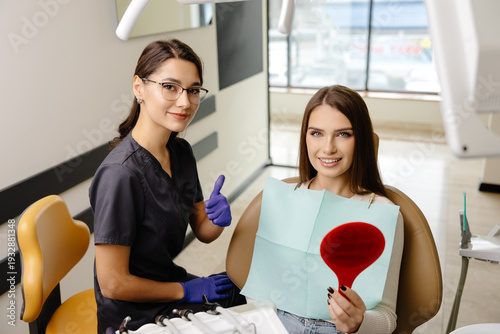 Woman is happy with results after oral hygiene and teeth whitening at dentist office. Patient is smiling and looking at the mirror