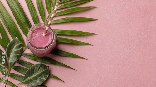 Overhead shot of a pink smoothie in a jar with straw, placed on a palm leaf against pink