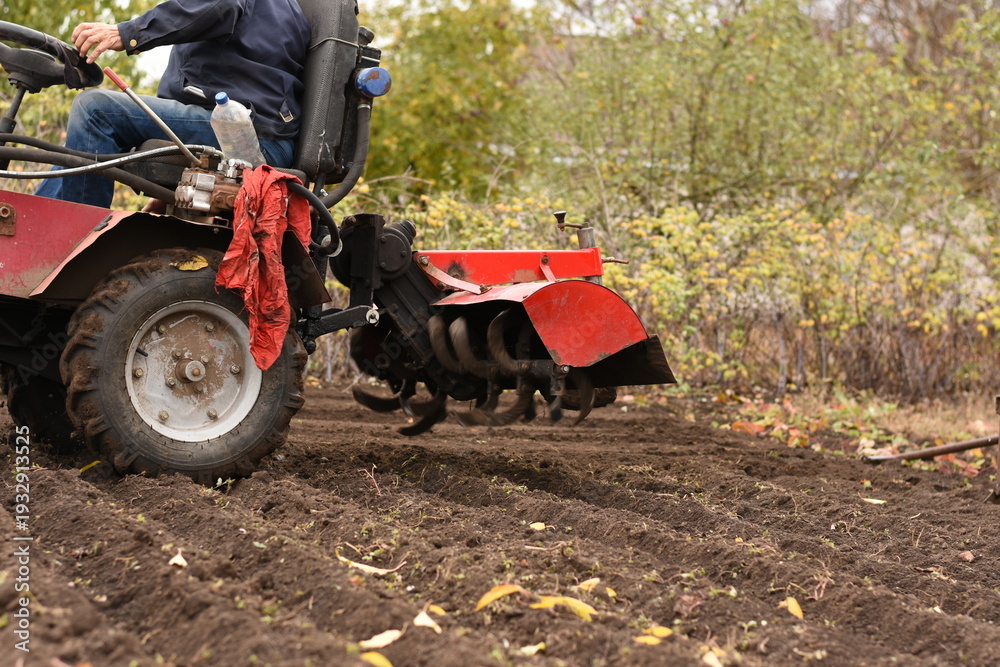 Obraz premium Man on red tractor, side view, close-up of rear part, plow lifted above soil, horizontal shot.