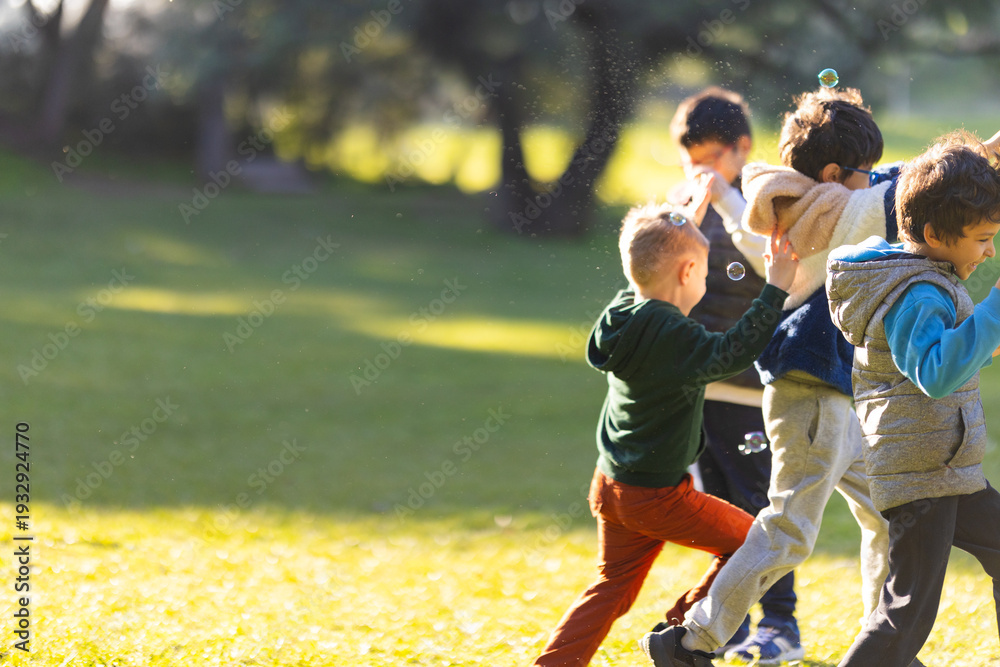 Obraz premium Happy boys playing together, chasing bubbles in park