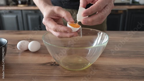 Mans hands cracking eggs into bowl to separate yolks from whites for sponge cake batter. Baking preparation and precise culinary technique.