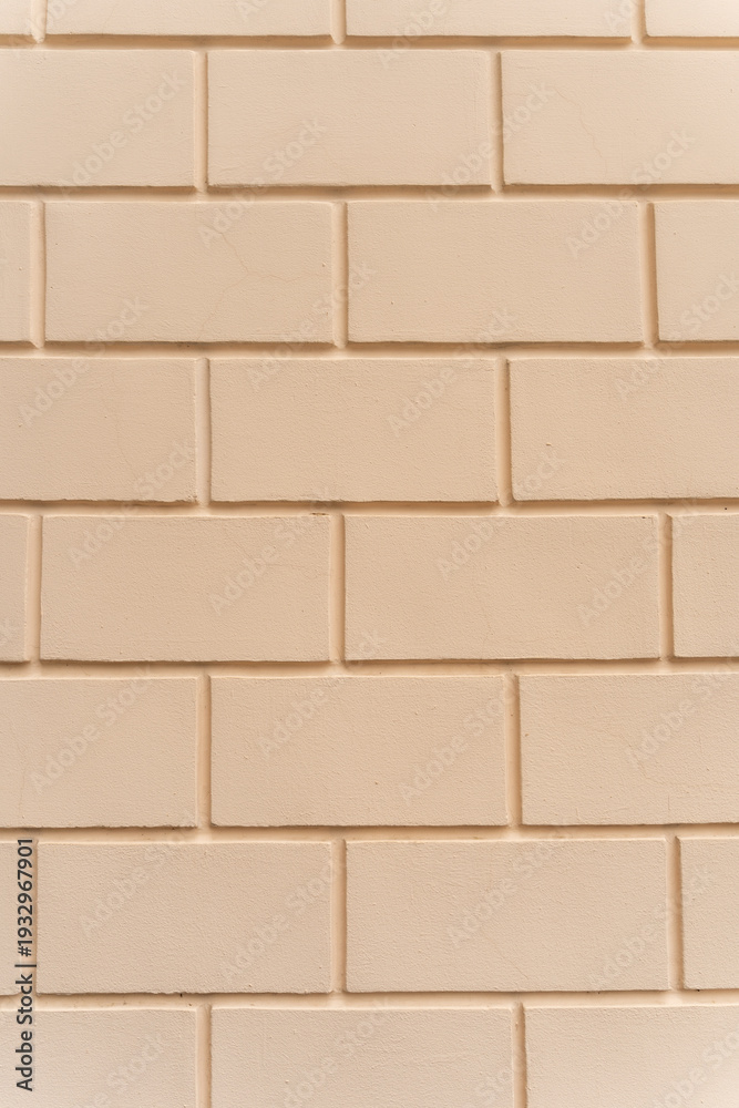 Fototapeta premium Pale yellow plaster wall with an imitation brick pattern forming a clean textured background. Decorative masonry-style surface with rectangular blocks arranged in a regular pattern.