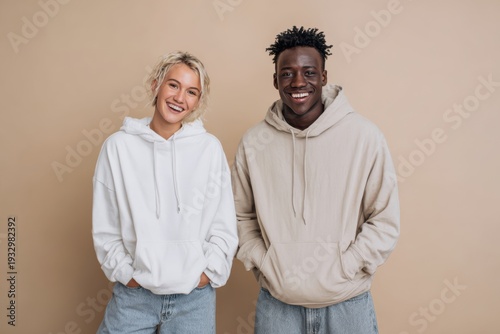 Two young friends wearing casual hooded sweatshirts standing side by side and smiling confidently against plain studio background