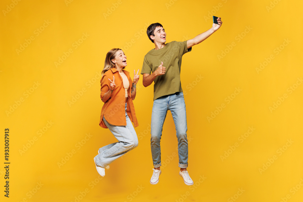 Fototapeta premium Full body young couple two friends family man woman wear casual clothes together do selfie shot on mobile cell phone post photo on social network jump high isolated on pastel plain yellow background.