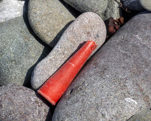 A close-up of an old weathered shotgun shell on a rocky beach.